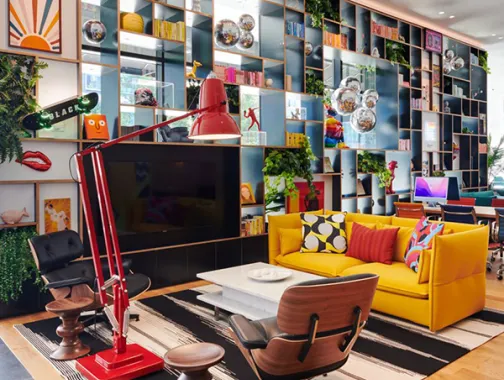 Colorful modern lounge at CitizenM Georgetown with a yellow sofa, red lamp, and floor-to-ceiling shelving.